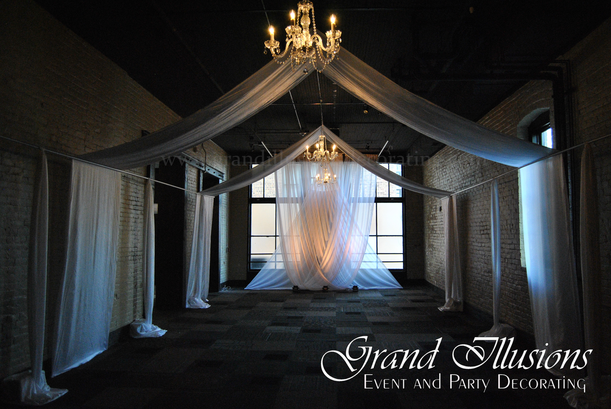 An elegantly decorated event space featuring draped white fabric and chandeliers, creating a romantic ambiance.